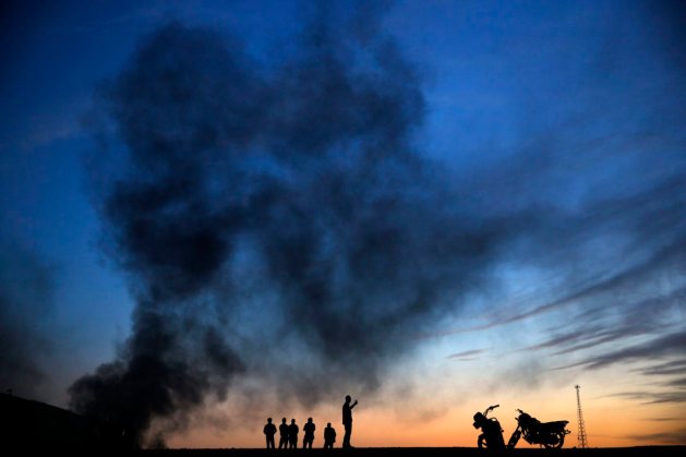 Kurdish refugees stand and walk on a hilltop as thick smoke rises from the Syrian town of Kobani during heavy fighting between Islamic State and Kurdish Peshmerga forces in Sanliurfa province, Turkey on Oct. 26, 2014.