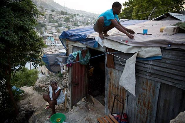 Nadain Javier repairs the leaking roof of his makeshift house in the earthquake-ravaged neighborhood of Campeche, in Port-au-Prince, Haiti, December 6, 2012. The Red Cross promised to build hundreds of new homes in Campeche but none have been built. (Photo: Damon Winter/The New York Times) 